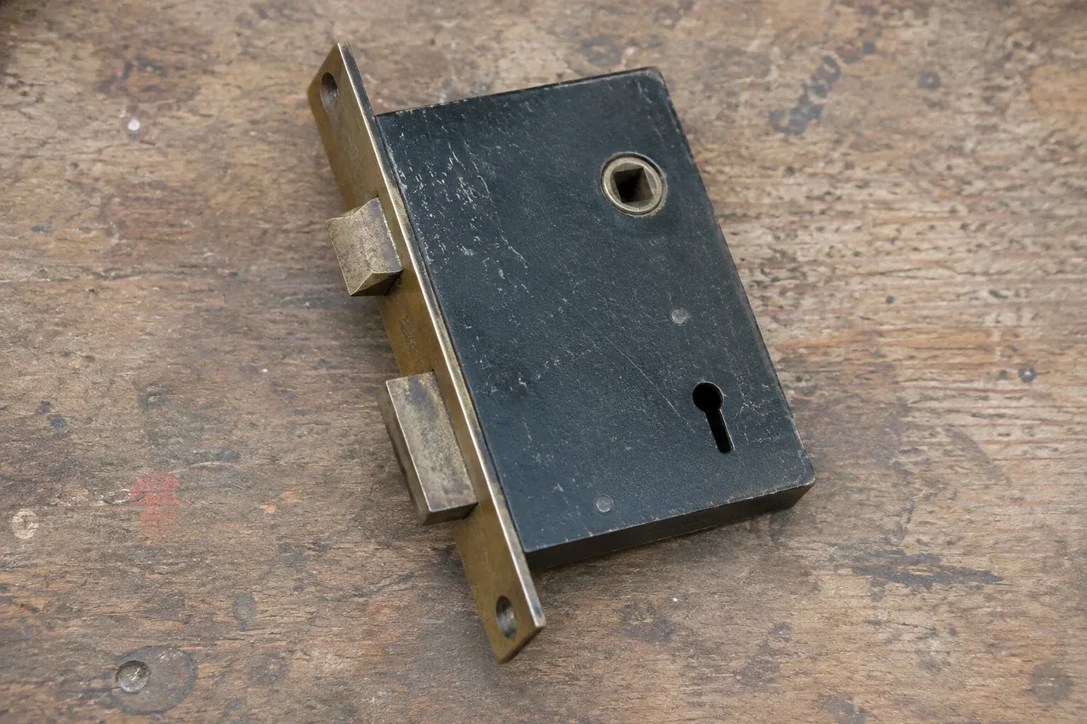Closed mortise lock case with spindle opening, keyhole, latch and deadbolt on a wooden workbench. — Vintage Mortise Lock Service, Burlington