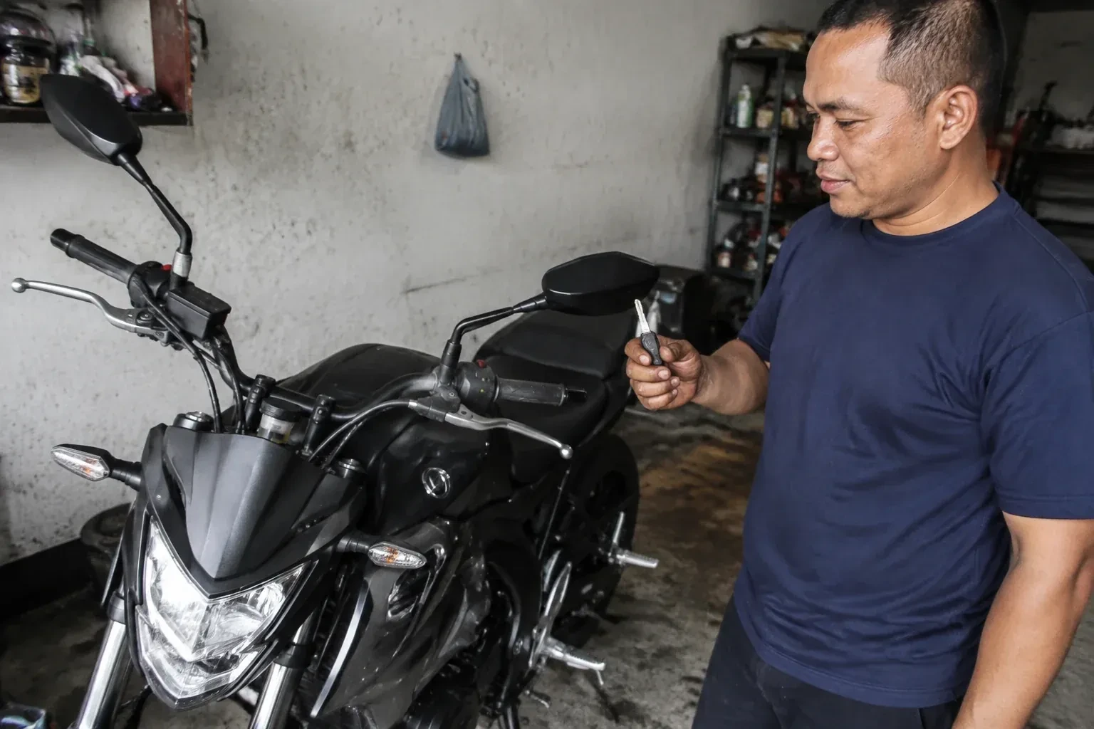 Person holding a key beside a black motorcycle in a garage. — Motorcycle & Scooter Keys, Burlington