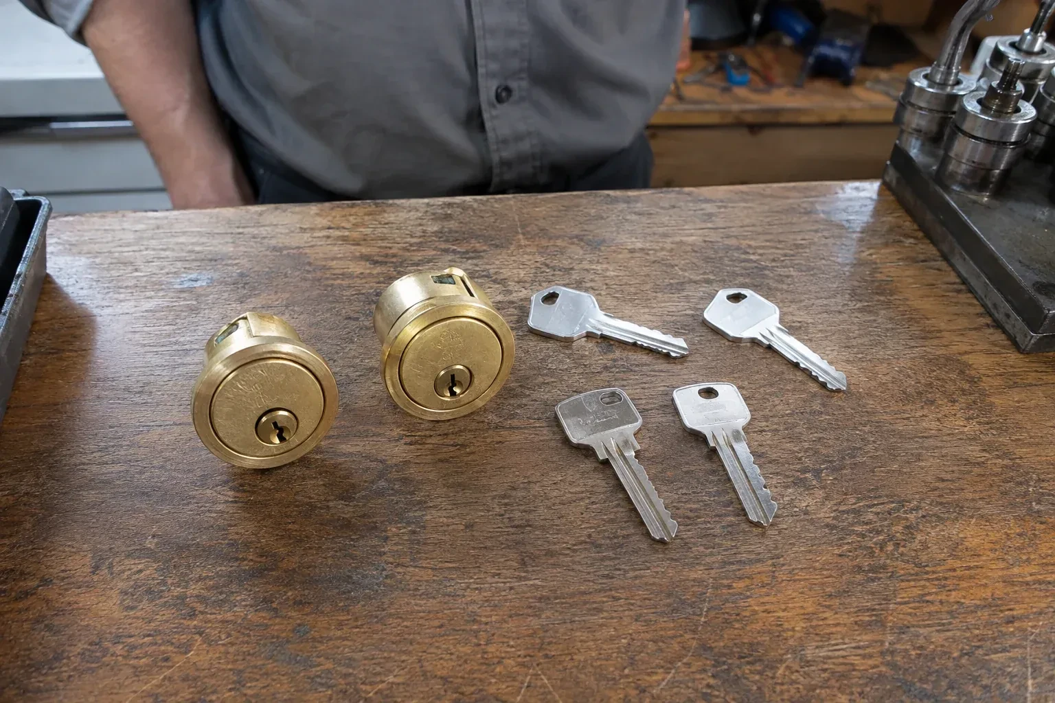 Two detached brass lock cylinders and four house keys on a wooden counter. — Lock Rekeying, Burlington